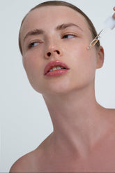 Woman applying a dropper of skincare product to her face against a white background